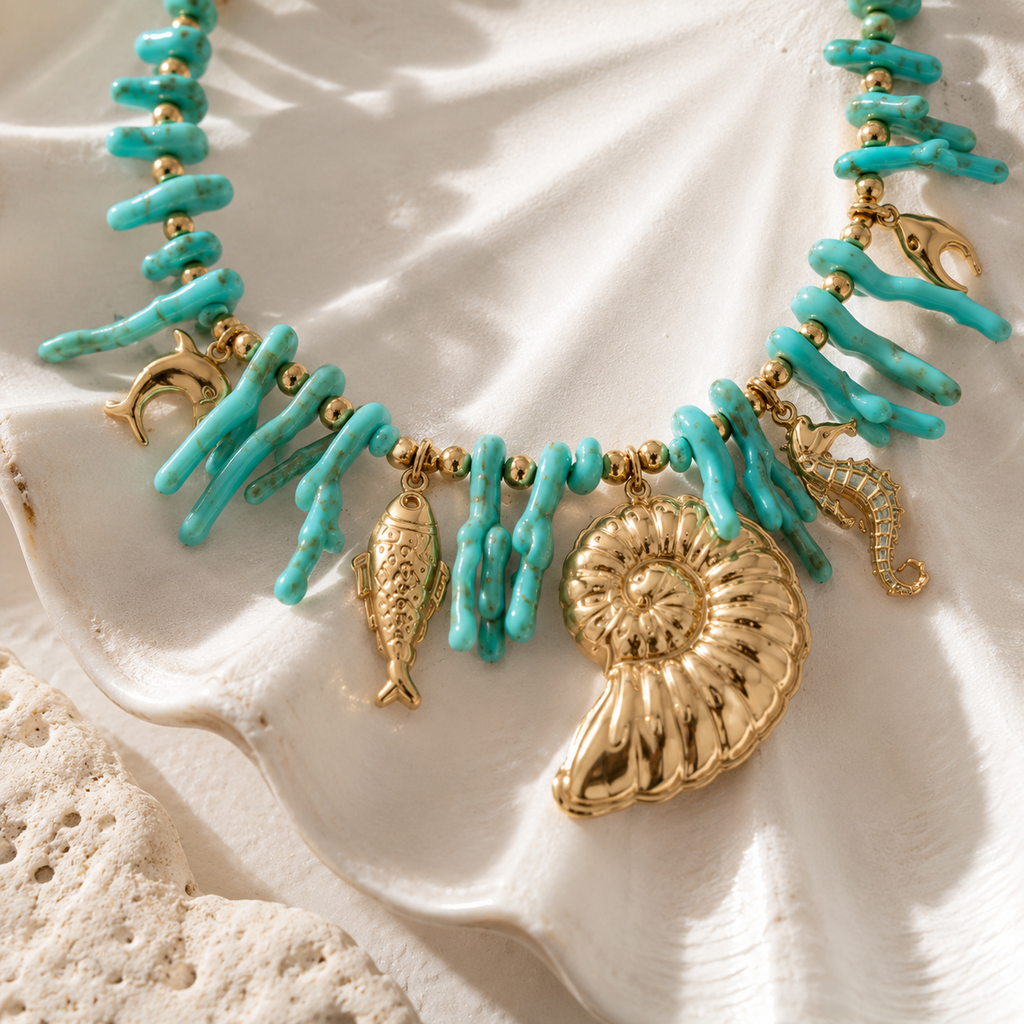 Aqua Charm Necklace Gold op beige steen met schelpen in luxe beach setting