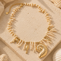 Coral Charm Necklace Gold op beige steen met schelpen in luxe beach setting